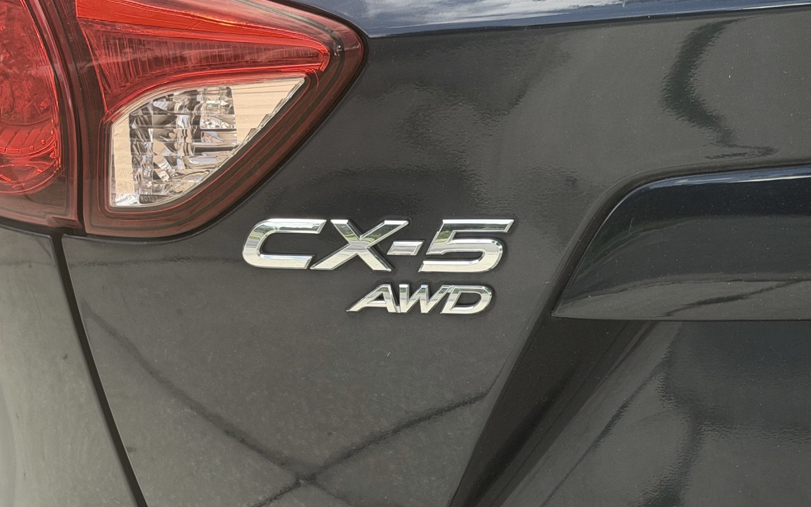 Chrome CX-5 AWD badge on the rear of a dark grey Mazda, beside the tail light