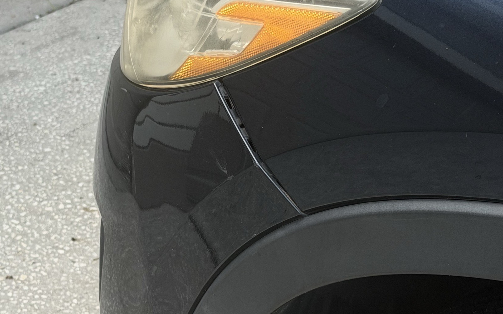 Front bumper cover separated from the fender on a dark grey SUV, leaving a wide uneven gap with the mounting clips visible inside it