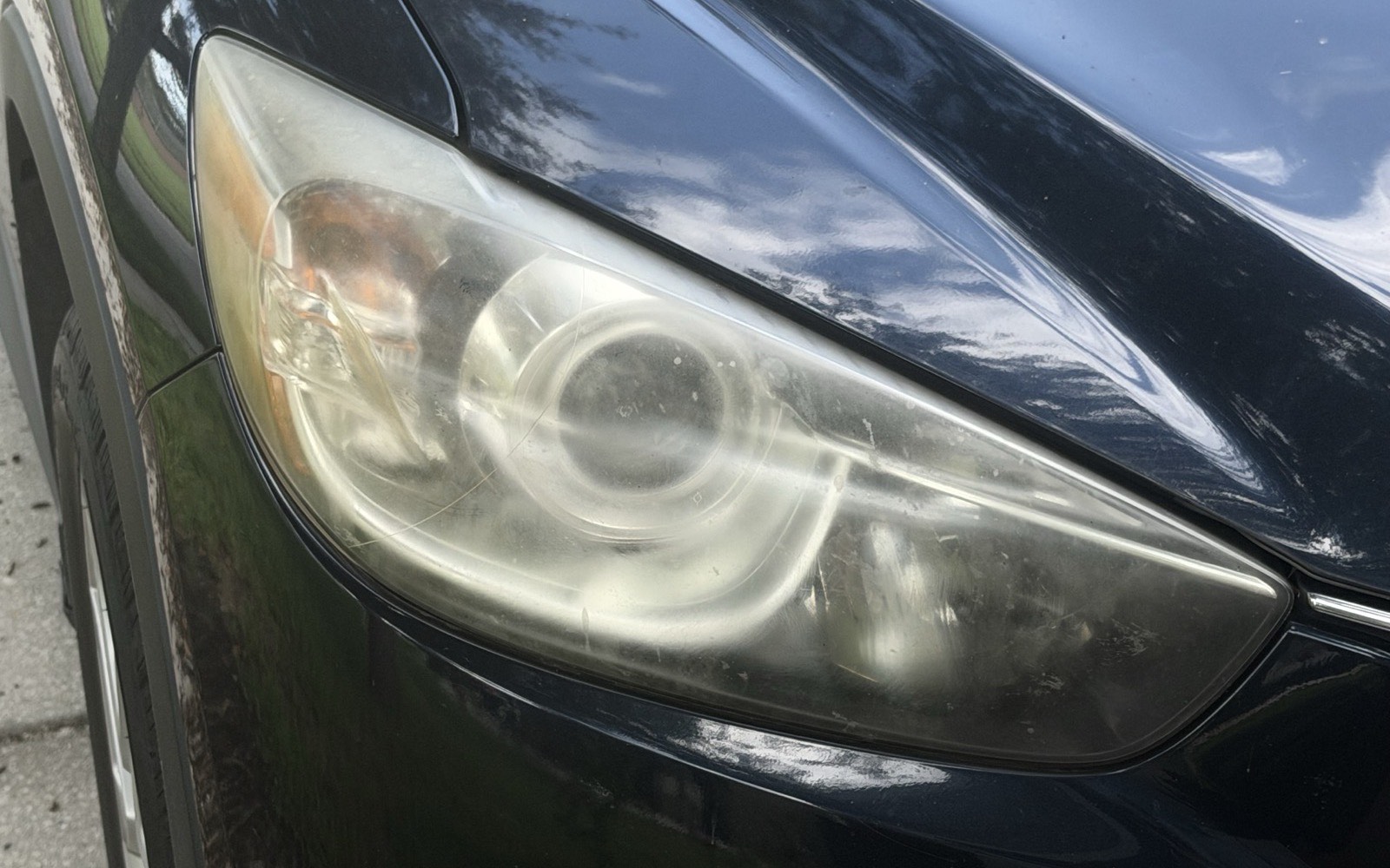 Headlight lens on a dark grey SUV, yellowed and clouded with oxidation