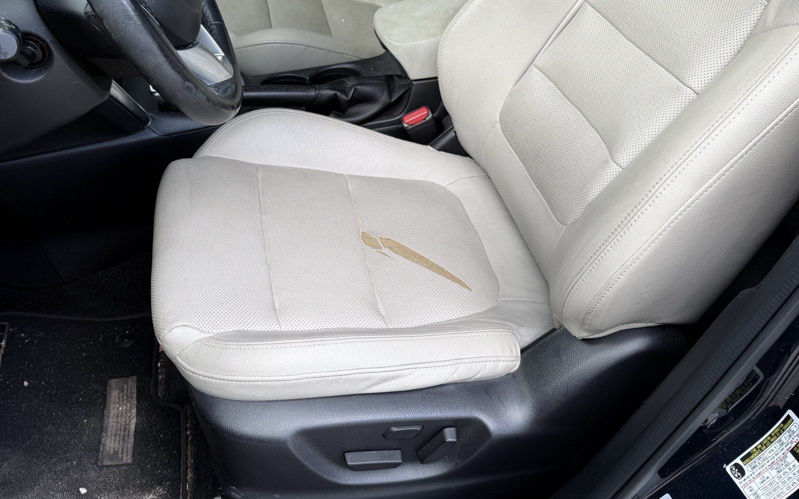 Split in the pale leather of a driver's seat cushion, with the foam backing visible through the tear